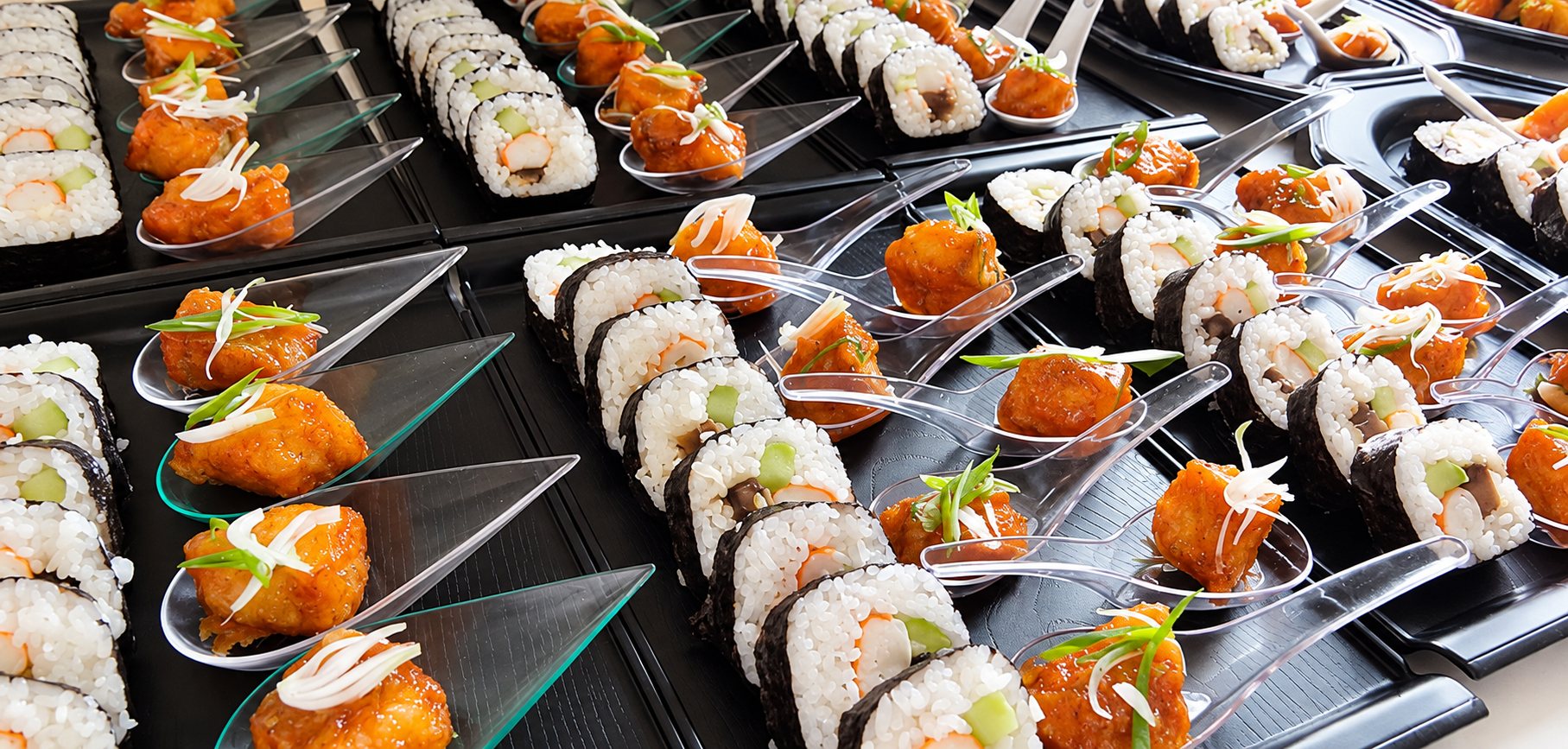 Sushis et bouchées de poulet caramélisé servis dans des cuillères sur plateaux noirs